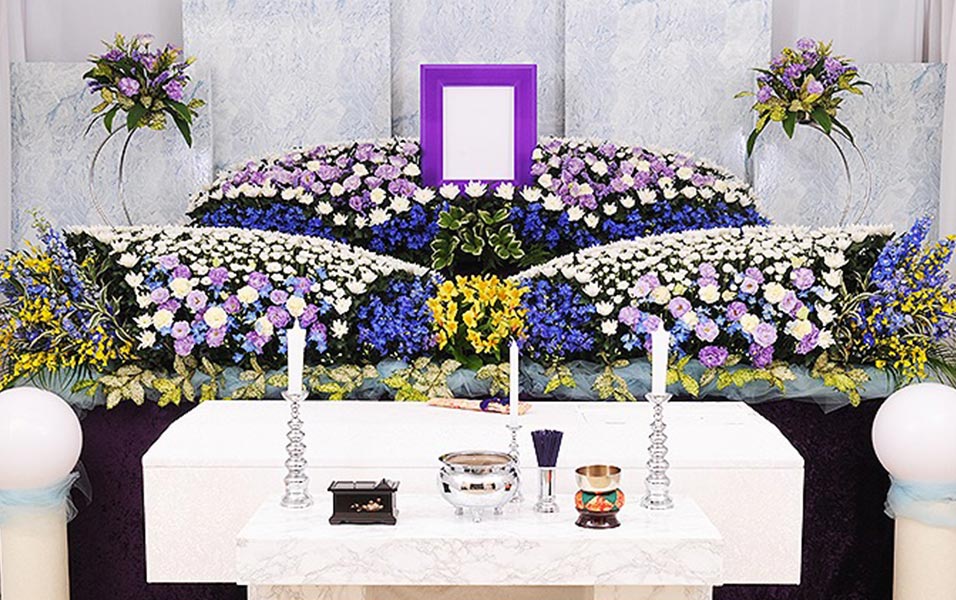 白、紫などの花で作られた祭壇の前には棺が置かれています